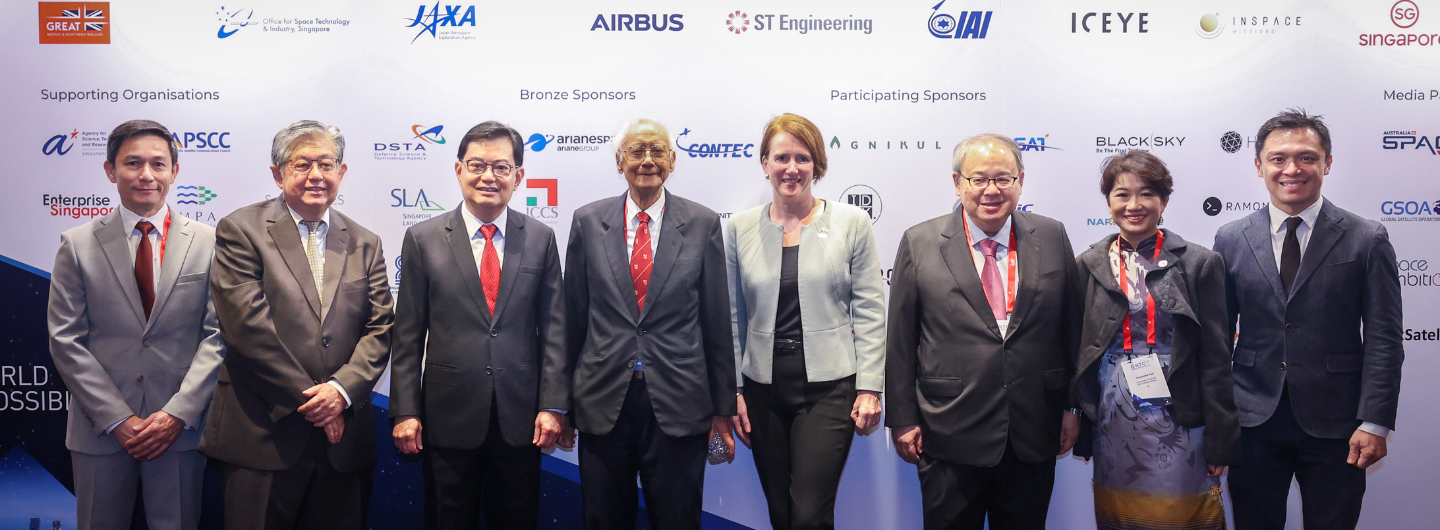 Group of people standing in front of a backdrop with logos of organizations and companies.